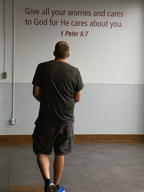 Program participant in front of wall with verse 1 Peter 5:7.